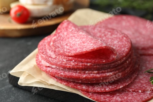 Preview: Slices of tasty smoked sausage on black table, closeup