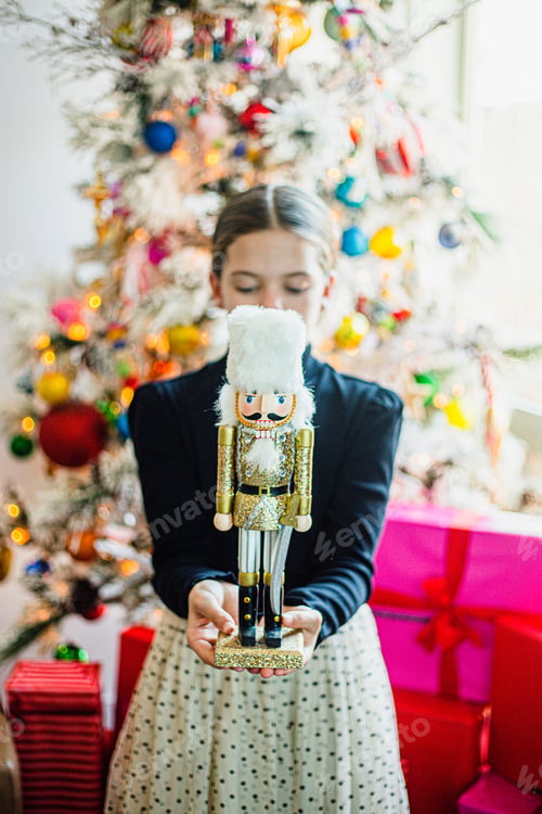 Preview: Girl holding a sparkly nutcracker in front of a Christmas tree