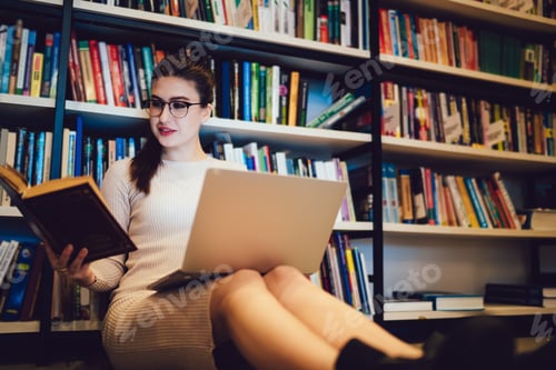 Preview: Dark haired woman in glasses reading book and using laptop