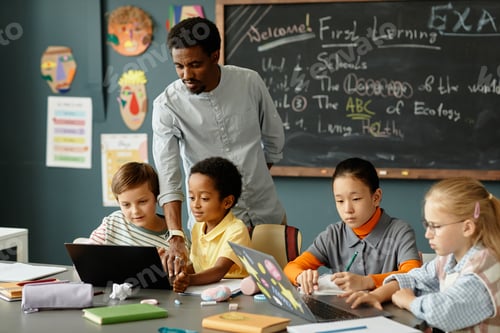 Preview: Children Using Laptops at Desk while Male Teacher Helping Kids in Classroom