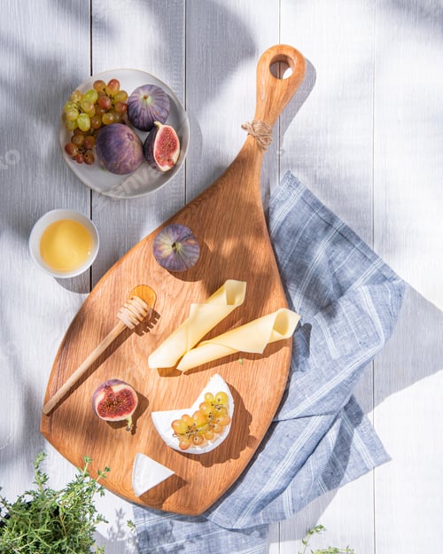 Preview: Assorted cheeses with figs, grapes and honey on a wooden board on white background with fresh herb.