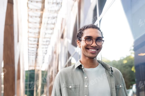 Preview: stylish african american man in eyeglasses and piercing smiling at camera on blurred bridge