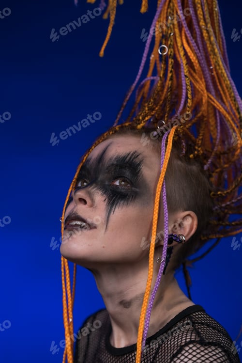 Preview: Cinematic portrait young woman with horror make-up painted on face and orange dreadlocks hairstyle