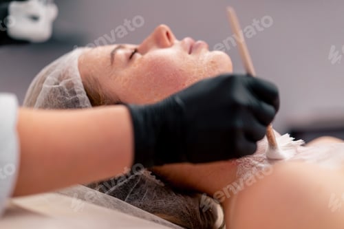 Preview: close-up beautician in gloves applies a mask on face neck of a client with a brush care for the skin