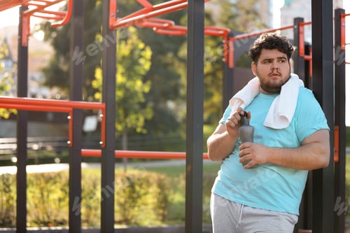 Preview: Young overweight man with bottle and towel on sports ground