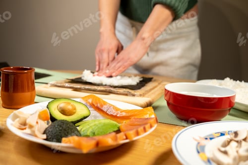 Preview: Closeup of a person making sushi with avocados, fish, and mushrooms on the table