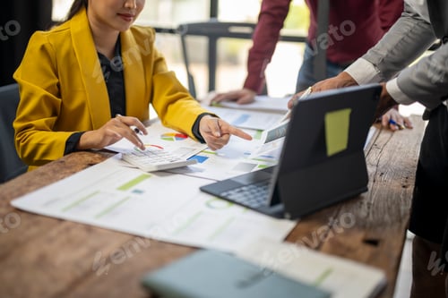 Preview: A woman in a yellow jacket is pointing at a laptop on a table.
