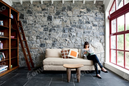 Preview: Woman sitting and reading on sofa of living room