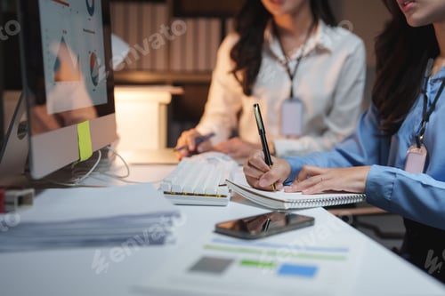 Preview: Businesswomen working late in office taking notes and analyzing charts on computer screen
