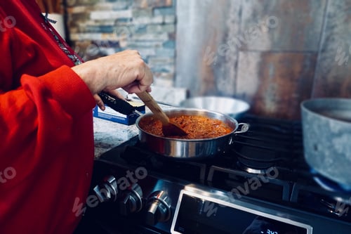 Preview: Woman stirring sauce in pan on stove in kitchen.