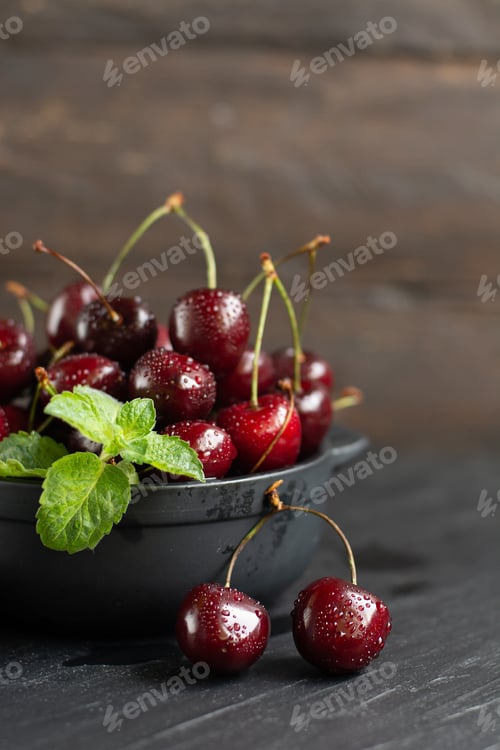 Preview: Fresh sweet cherries with water drops in bowl on dark rock table.