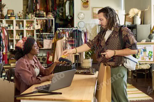 Preview: Young Caucasian Man Paying Black Woman Cashier at Thrift Shop Counter