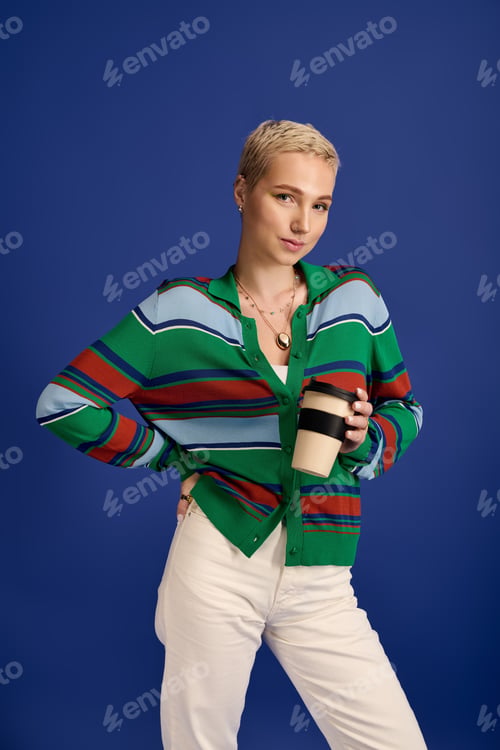 Preview: Fashionable young woman enjoying coffee against a vibrant blue backdrop with style and confidence