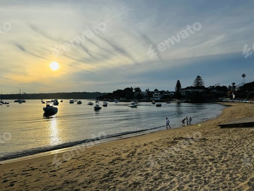 Preview: Sunset view over a beach with boats anchored in the calm water and people walking along the shore.
