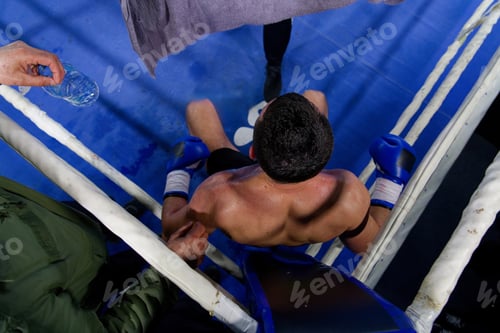 Preview: Top view of cornered boxer receives strategic advice from trainer during intense bout.