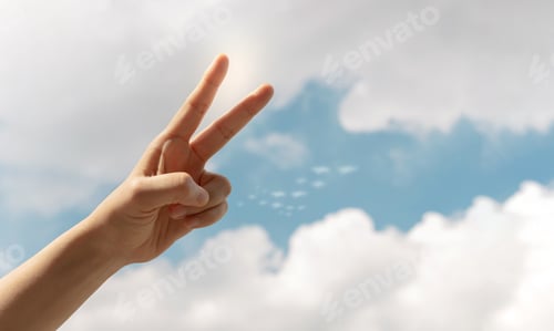 Preview: Hand making a peace sign against a bright blue sky, symbolizing peace, hope, freedom
