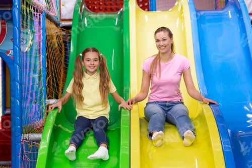 Preview: Positive millennial mother and her teenage daughter riding slide together at kids amusement centre