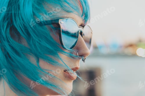 Preview: Portrait of a young female with blue and pink hair wearing sunglasses with a blurred background