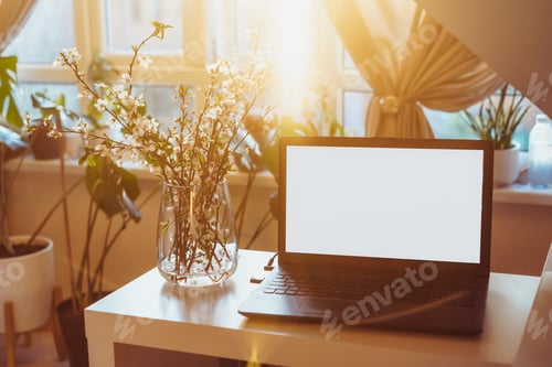Preview: A home workplace with a white screen laptop for mockup and blooming branches in a vase on the sunset