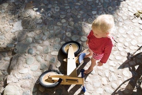 Preview: Overhead view of female toddler and wooden bicycle on cobbles