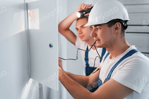 Preview: Two young male electricians works indoors together. Using flashlight