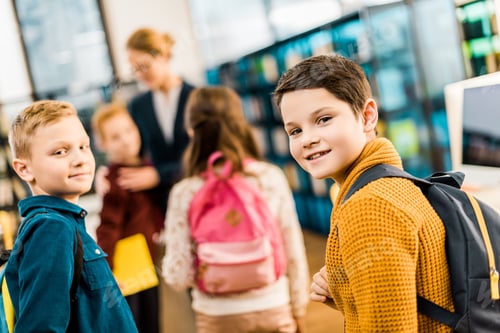 Visualização: adoráveis estudantes com mochilas olhando para a câmera na biblioteca