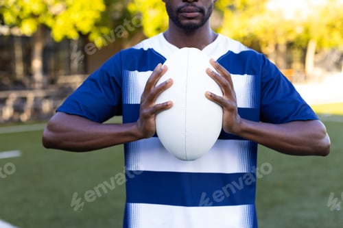 Preview: African American young male athlete holding a rugby ball, standing on field outdoors