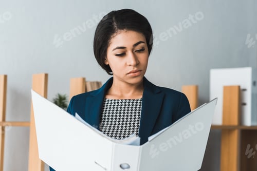 Preview: Confident businesswoman looking at folder in modern office