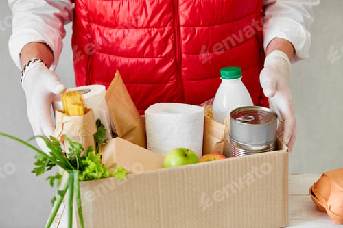 Preview: Volunteer in the protective medical mask and gloves putting food In donation box.