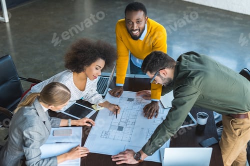 Preview: high angle view of multicultural businesspeople looking at blueprint in workspace