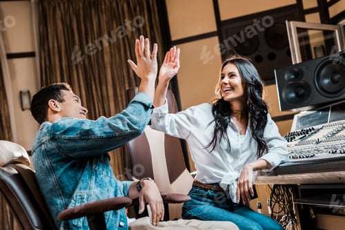 Preview: two cheerful multicultural sound producers giving five in recording studio