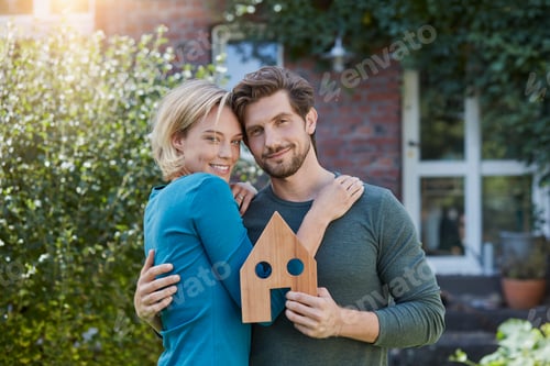 Preview: Portrait of happy couple in front of their home with house model