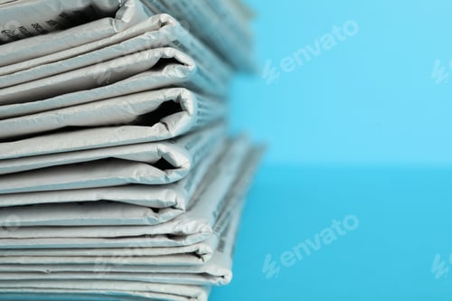 Preview: Stack of newspapers on light blue background, closeup with space for text. Journalist's work