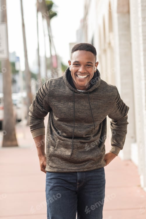 Preview: pleased african american man in wireless earphones listening music on street in Miami