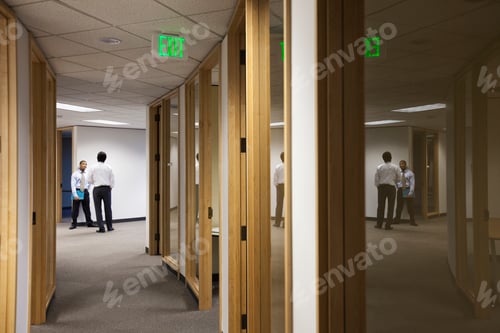 Preview: Two business men standing and talking at the end of an office hallway.