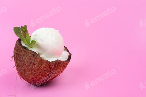Preview: Vanilla ice cream balls in fresh coconut halves, decorated with mint leaves on a pink background