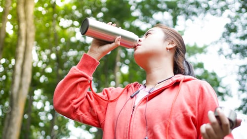 Preview: Asian women drinking water after exercise on green nature forest background