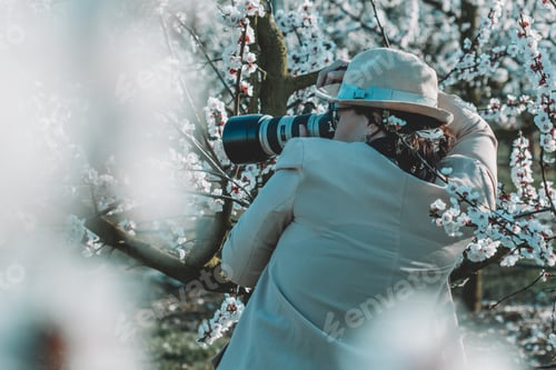 Preview: young woman photographer during work. photography in blooming sakura gardens. early spring.