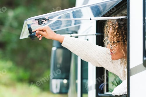 Preview: One woman opening camper window with green mountain forest in background. Concept of travel