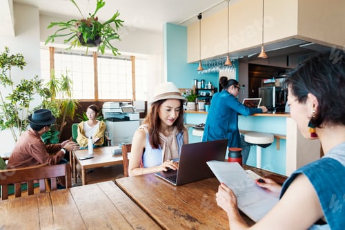 Preview: Group of young Japanese professionals working on laptop computers in a co-working space.