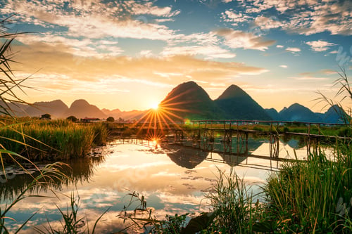 Preview: Sunset over mountain with villager pushing bicycle on wooden bridge over the river in countryside