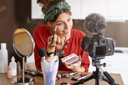 Preview: Portrait of happy young female beauty blogger using big palette and brush, applying eyeshadow while