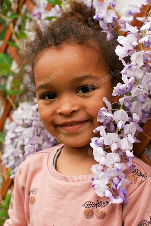 Preview: Portrait of a toddler girl in front of purple wisteria flowers - petals pink mixed race diversity