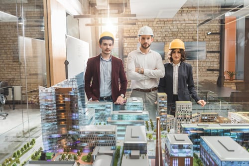 Preview: team of architects in hard hats in front of miniature town model at office