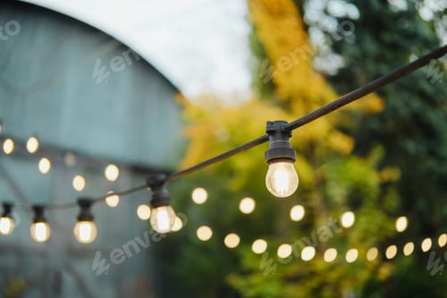 Preview: Warm outdoor string lights glowing softly at dusk on a patio, garden background.