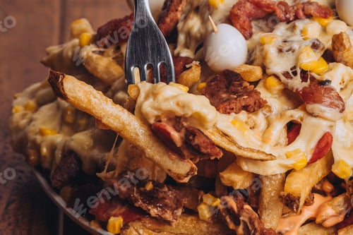 Preview: Closeup shot of a dish with french fries, sausages topped with cheese and corn on a wooden table.