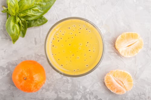 Preview: Glass of tangerine orange colored drink with basil seeds on a gray concrete background. Top view