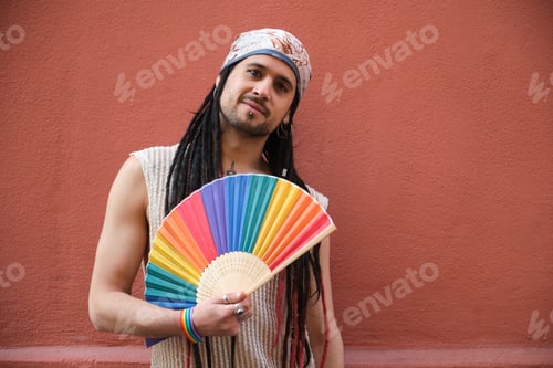 Preview: Young man holding rainbow hand fan celebrating gay pride supporting LGBT community