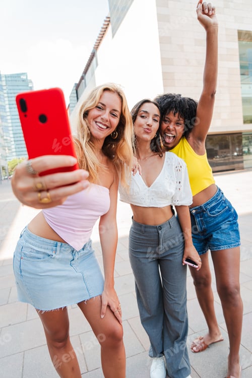 Preview: Vertical. group of three happy young women taking a selfie outdoors, smiling and enjoying a fun