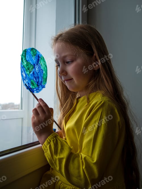 Preview: Cute little girl painting planet on window at home Happy Earth Day April 22 greeting message